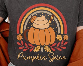 May include: Dark grey t-shirt with a pumpkin spice design. The graphic features a pumpkin with whipped cream, a rainbow, and the words "Pumpkin Spice". Autumn-themed clothing.