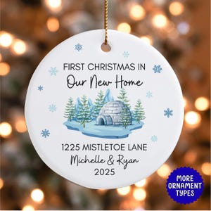 May include: A white ceramic Christmas ornament with the text "First Christmas In Our New Home." It features an igloo and pine tree design. The ornament also includes the address "1225 Mistletoe Lane," the names "Michelle & Ryan," and the year "2025."