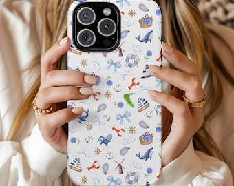 Puede incluir: Una funda de teléfono blanca con un patrón de temática náutica. El diseño incluye veleros, anclas, langostas, ballenas y lazos en azul, rojo y verde. La funda la sostiene una persona.