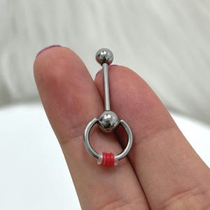 May include: Silver barbell with a ring on one end. The ring has red and white rubber o-rings.