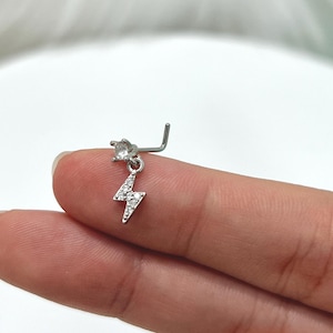 May include: A silver nose ring with a dangling lightning bolt charm. The charm is encrusted with clear rhinestones.