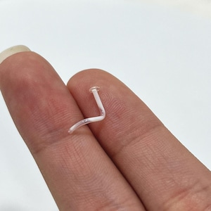 Pode incluir: Um piercing de nariz de plástico transparente com um design curvo em forma de L.