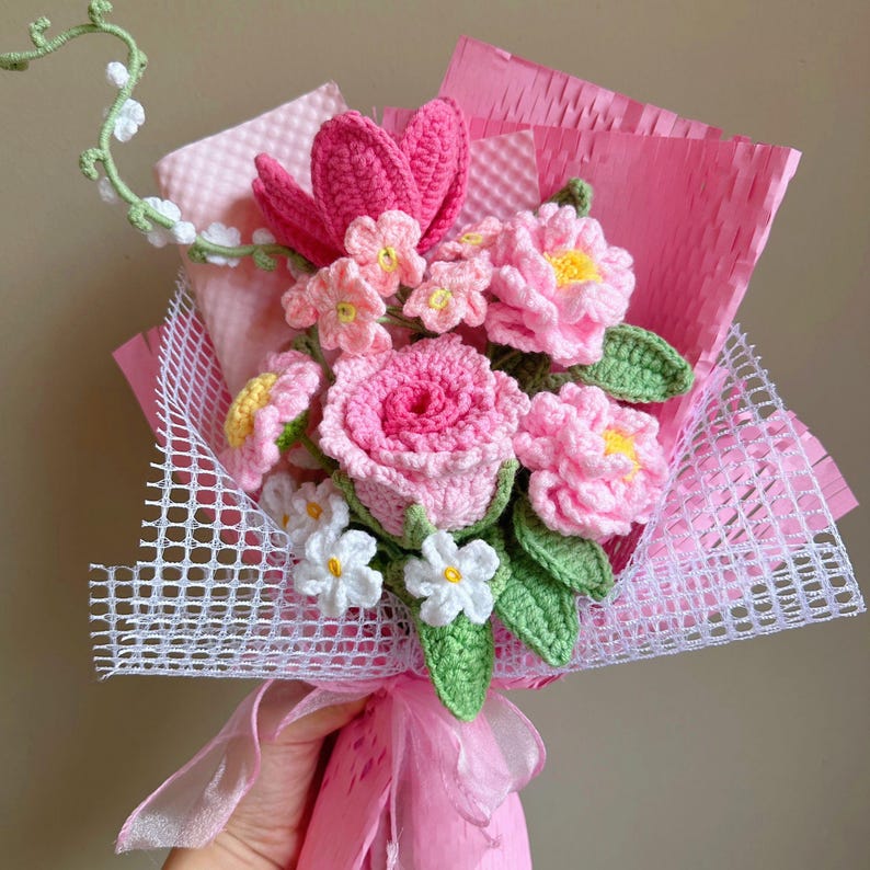 K&ouml;nnte beinhalten: Ein geh&auml;kelter Strau&szlig; aus rosa und wei&szlig;en Blumen, verpackt in rosa Seidenpapier und wei&szlig;em Netz.