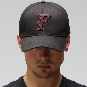 Op de afbeelding: Een zwarte baseballpet met een rode, omrande hoofdletter "F" geborduurd op de voorkant.