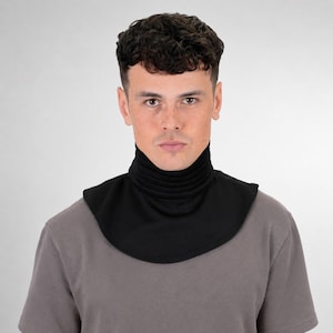 May include: A black mock neck dickey featuring a ribbed collar and a rounded hem that covers the upper chest and neck area. The accessory is worn over a plain grey short-sleeved t-shirt, providing a layered appearance without the bulk.