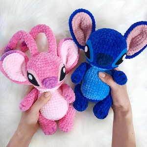 May include: Two handmade crochet plush toys featuring large ears and oval eyes. One plush is bright pink with a lighter pink belly, while the other is deep blue with a lighter blue chest. Both have soft, textured yarn surfaces and rounded limbs.