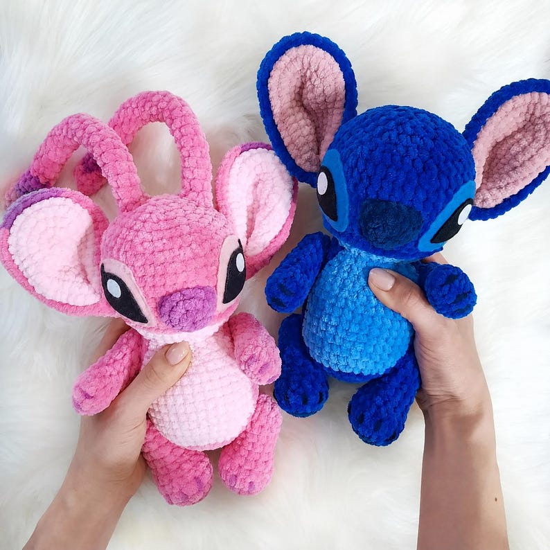 May include: Two handmade crochet plush toys featuring large ears and oval eyes. One plush is bright pink with a lighter pink belly, while the other is deep blue with a lighter blue chest. Both have soft, textured yarn surfaces and rounded limbs.