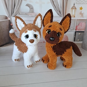 May include: Two plush dog toys made of soft yarn. The left toy is white and brown with large dark eyes and a small nose. The right toy is brown and dark brown with large dark eyes and a black nose. Both toys have pointed ears and textured fur.