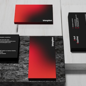 May include: Business cards with a modern design. The cards feature a gradient of red to black, with the company name "blaqden" and contact information. The cards are displayed on a white and gray surface.