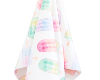 May include: A white hand towel with a watercolor print of colorful popsicles. The towel is hanging from a hook.