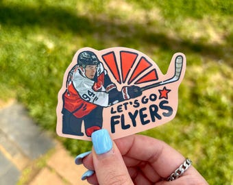 May include: A sticker depicting a hockey player in red, white, and black, with the words "LET'S GO FLYERS". The sticker has a pink background and a hockey stick design.