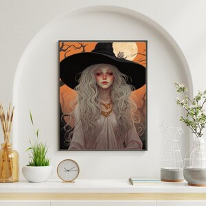 May include: A framed art print depicting a witch with long, silver hair, wearing a black hat and a white dress. A cat sits on the hat, with a full moon and bare tree branches in the background. The artwork has an orange and black colour scheme.