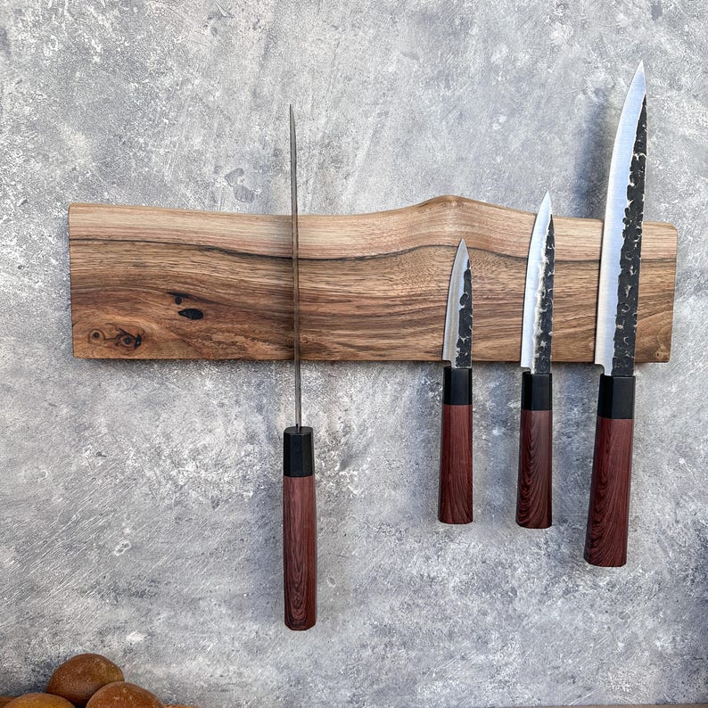 May include: A wooden knife holder with a natural edge, displaying five knives. The knives have dark wooden handles, black accents, and silver blades. The holder is mounted on a grey textured wall.