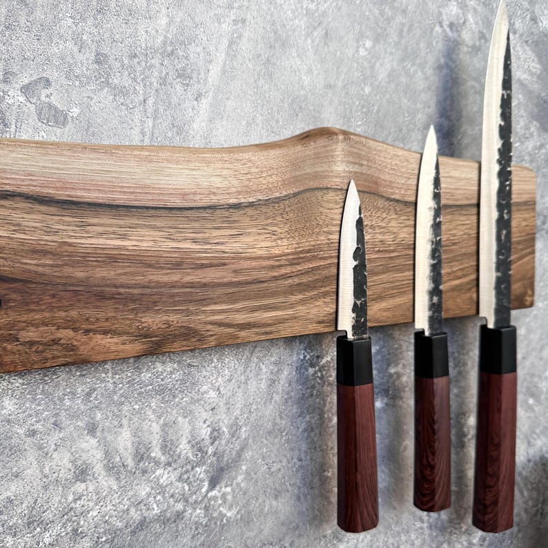 May include: A wooden knife holder displaying four knives. The holder is made of dark wood with a natural edge. The knives have dark wood handles, black bolsters, and silver blades. The blades have a textured finish.