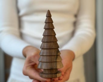 Op de afbeelding: Een houten kerstboomversiering gemaakt van gestapelde ringen van donkerbruin hout. De boom is ongeveer 25 cm hoog en heeft een eenvoudig, elegant ontwerp.