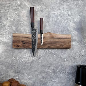 May include: A wooden knife holder with two knives. The holder is made of dark wood and has a natural edge. The knives have dark brown handles and textured blades. The larger knife is approximately 30 cm long.