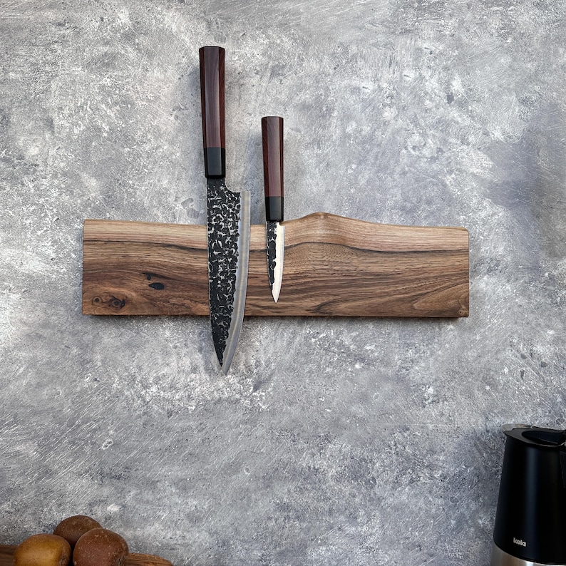 May include: A wooden knife holder with two knives. The holder is made of dark wood and has a natural edge. The knives have dark brown handles and textured blades. The larger knife is approximately 30 cm long.