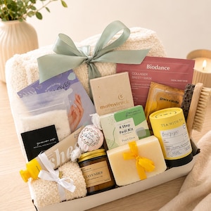 May include: A gift box containing a cream-coloured fuzzy blanket with a sage green ribbon, a Biodance collagen sheet mask, Grace & Stella eye masks, a Moonstruck candle, a 4 Step Pedi Kit, a lavender candle, a bar of soap, and Tea With Tae tea.