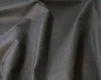 May include: A close-up of a dark gray fabric with a smooth texture. The fabric is folded and draped, creating soft folds and wrinkles.
