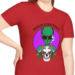Puede incluir: Camiseta roja con un gráfico de un alienígena verde fumando, una calavera y las palabras "MIND CONTROL" en un círculo morado. El alienígena lleva un arnés. La camiseta la lleva una persona.