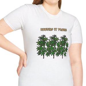 Puede incluir: Camiseta blanca con un diseño de hojas de cannabis verdes y el texto "KEEPING IT FRESH" en dorado. La camiseta es de cuello redondo.