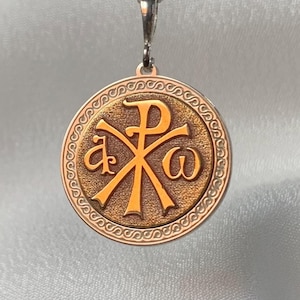 Può includere: Una collana con un ciondolo rotondo in oro e argento, decorata con un medaglione rotondo dorato che rappresenta il simbolo Chi Rho, un simbolo cristiano che rappresenta Cristo.