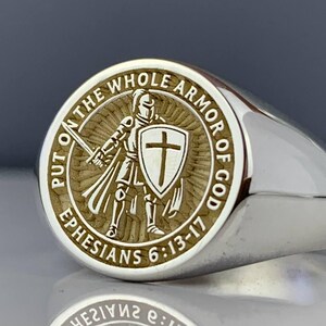 May include: Silver signet ring with an engraved design. The ring has a circular emblem depicting a knight with a sword and shield, encircled by the words "PUT ON THE WHOLE ARMOR OF GOD" and "EPHESIANS 6:13-17".