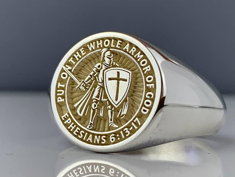 May include: Silver signet ring with an engraved design. The ring has a circular emblem depicting a knight with a sword and shield, encircled by the words "PUT ON THE WHOLE ARMOR OF GOD" and "EPHESIANS 6:13-17".