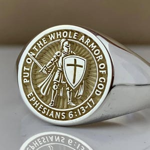 May include: Silver signet ring with an engraved design. The ring has a circular emblem depicting a knight with a sword and shield, encircled by the words "PUT ON THE WHOLE ARMOR OF GOD" and "EPHESIANS 6:13-17".