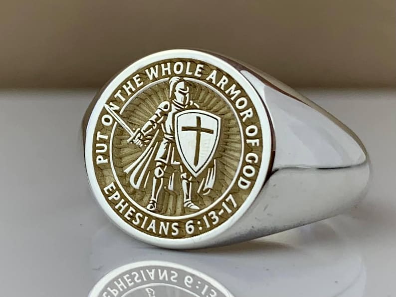 May include: Silver signet ring with an engraved design. The ring has a circular emblem depicting a knight with a sword and shield, encircled by the words "PUT ON THE WHOLE ARMOR OF GOD" and "EPHESIANS 6:13-17".