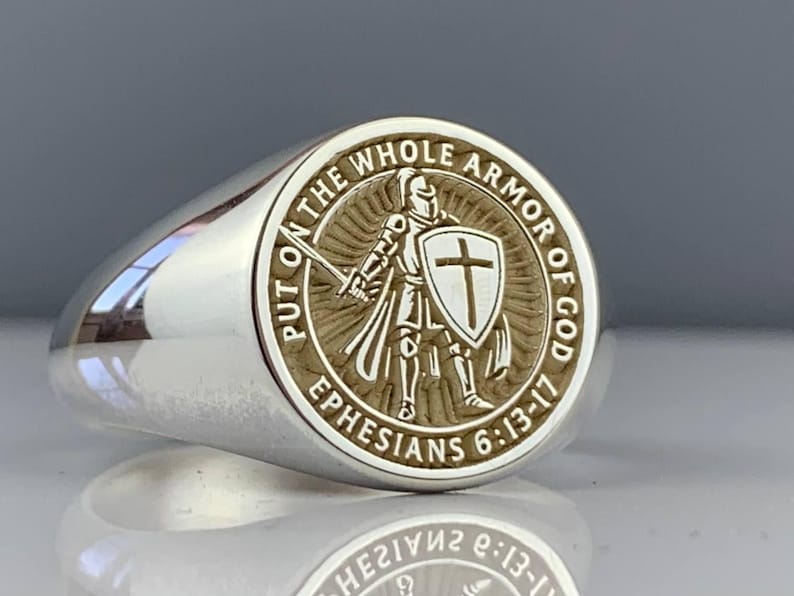 May include: Silver ring with a detailed circular emblem. The emblem features a knight with a sword and shield, surrounded by the text "PUT ON THE WHOLE ARMOR OF GOD" and "EPHESIANS 6:13-17".
