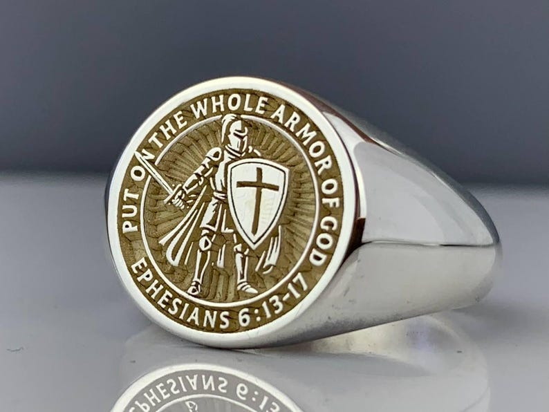 May include: Silver signet ring with an engraved design. The ring showcases a knight with a sword and shield, encircled by the words "PUT ON THE WHOLE ARMOR OF GOD" and "EPHESIANS 6:13-17".