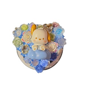 Puede incluir: Artículo decorativo con un personaje de perro de dibujos animados sentado en una nube azul, rodeado de flores azules, blancas e iridiscentes. Incluye un cristal en forma de corazón. El artículo está sobre un fondo blanco.
