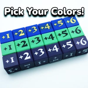 May include: A selection of coloured dice with white numbers and symbols, arranged in rows. The dice are blue, green, and purple, with the text "Pick Your Colors!" above them. Each die has a number from +1 to +6.