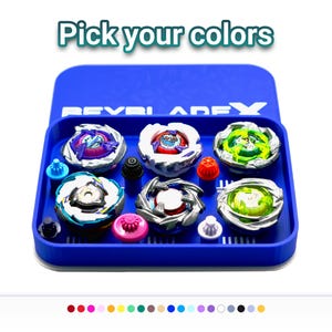 Puede incluir: Un contenedor azul con varias peonzas de colores. Las peonzas presentan diversos diseños y colores, incluyendo morado, verde, blanco y plateado. El texto "Pick your colors" se muestra encima de las peonzas.