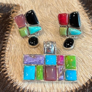 May include: A jewelry set consisting of a rectangular pendant and two matching earrings, each featuring a mosaic of inlaid stones in shades of turquoise, black, lime green, pink, purple, and red, set within a silver-toned metal frame.