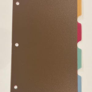 May include: A brown binder with colorful tab dividers. The tabs are in shades of orange, pink, teal, and blue. The binder has three holes for insertion into a ring binder.