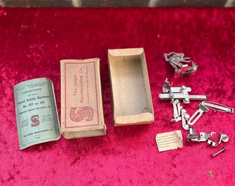 May include: A vintage Singer sewing machine accessory kit. The kit includes a box, instruction booklet, and various metal attachments. The box is tan with red text and a Singer logo. The instruction booklet is green and white.