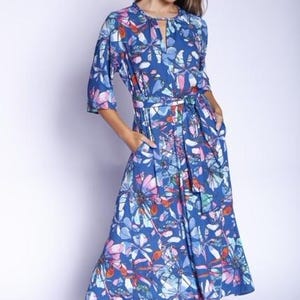 May include: A blue maxi dress with a floral print featuring butterflies and flowers in shades of pink, blue, and orange. The dress has a tie belt and a keyhole neckline.