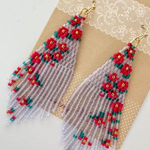 Może przedstawiać: Para długich, koralikowych kolczyków z geometrycznym wzorem. Kolczyki są wykonane z przezroczystych, białych, różowych i zielonych koralików. Kolczyki wiszą na złotych haczykach.