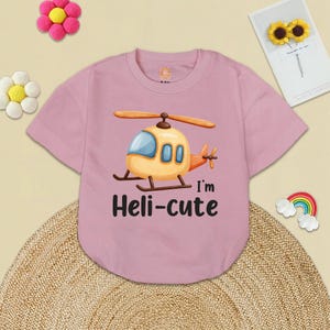 May include: Pink short-sleeved t-shirt with a cartoon helicopter and the text "I'm Heli-cute".