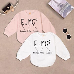 May include: Two long-sleeved shirts with a playful twist on Einstein's famous equation. The pink shirt and the white shirt both feature the equation "E=MC2" with the words "Energy", "Milk", and "Cuddles" written below.