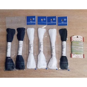 May include: A collection of embroidery floss in various colors. The image shows several spools of black and white thread, along with a multi-colored spool. Each spool is labeled with a number and brand information.