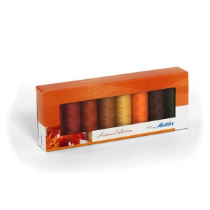 May include: A box of eight spools of thread in autumn colors. The spools are arranged in a row and are labeled "Autumn Collection". The box is made of cardboard and has a clear plastic window.