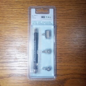May include: A roller set-diamonds kit by Walnut Hollow. The kit includes a black handle and three interchangeable metal roller heads. The packaging is clear plastic with a blue backing and the text "METAL" and "roller set-diamonds".
