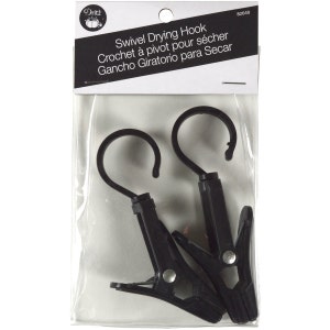 May include: Two black plastic swivel drying hooks with a metal clip. The hooks are packaged in a clear plastic bag with a white label that reads "Swivel Drying Hook Crochet à pivot pour sécher Gancho Giratorio para Secar".
