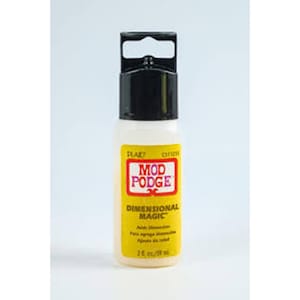 May include: A bottle of Mod Podge Dimensional Magic, a clear, glossy dimensional adhesive. The bottle has a black cap with a handle and a yellow label with red and white text. The label reads "Mod Podge Dimensional Magic" and "2 fl oz / 59 ml".