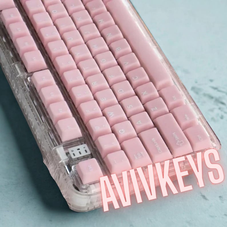 May include: A close-up of a pink mechanical keyboard with white lettering. The keyboard has a clear plastic case. The text "AVIVKEYS" is displayed in pink across the bottom of the keyboard.