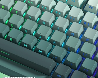 Puede incluir: Primer plano de un teclado mecánico de color verde azulado y gris con retroiluminación azul y verde. El teclado tiene una variedad de teclas, incluidas teclas de función, teclas numéricas y teclas de letras. El teclado está etiquetado como "AVIVKEYS".