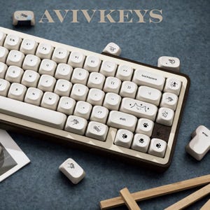 May include: A white and brown mechanical keyboard with custom keycaps. The keycaps feature various illustrations, including paw prints and a cat face. The keyboard has the text "AVIVKEYS" at the top.